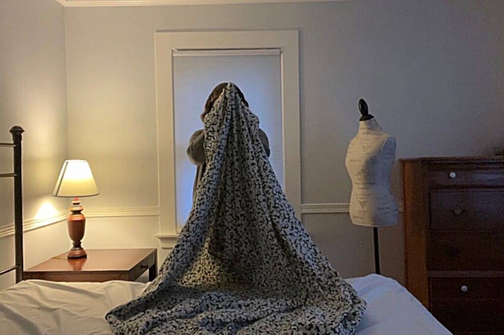 A mannequin on a bed, demonstrating how to fold a fitted sheet.