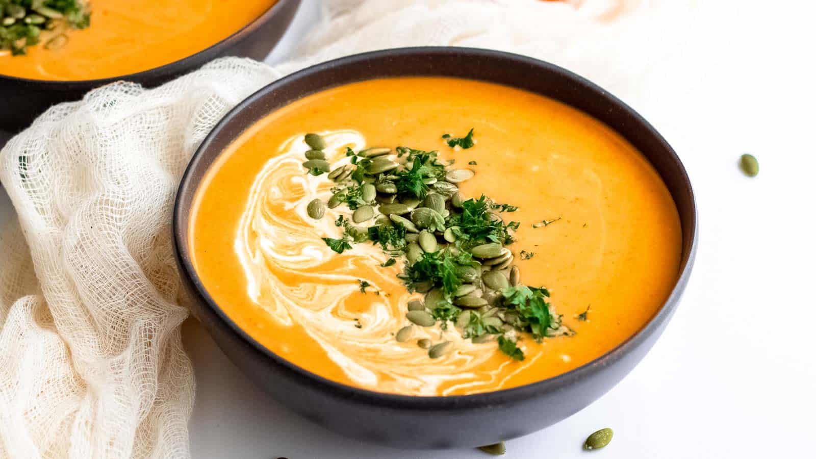 Two bowls of curry pumpkin soup with coconut cream and pumpkin seeds.