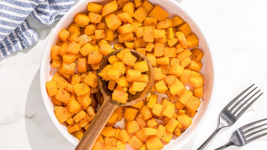 Sautéed butternut squash in a white bowl with a wooden spoon.