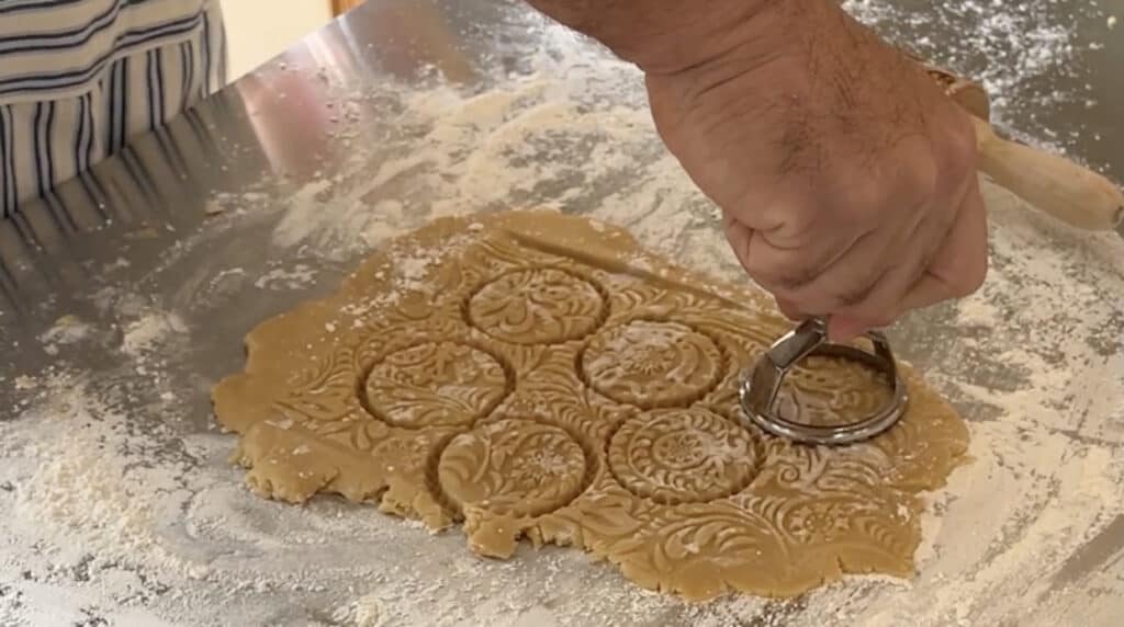 A person is using an embossed rolling pin to make cookies.