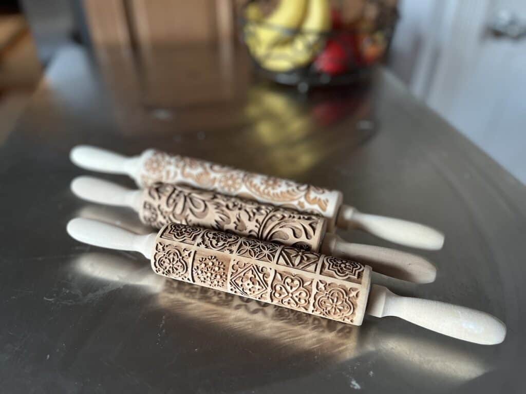 Three wooden embossed rolling pins on a counter top.