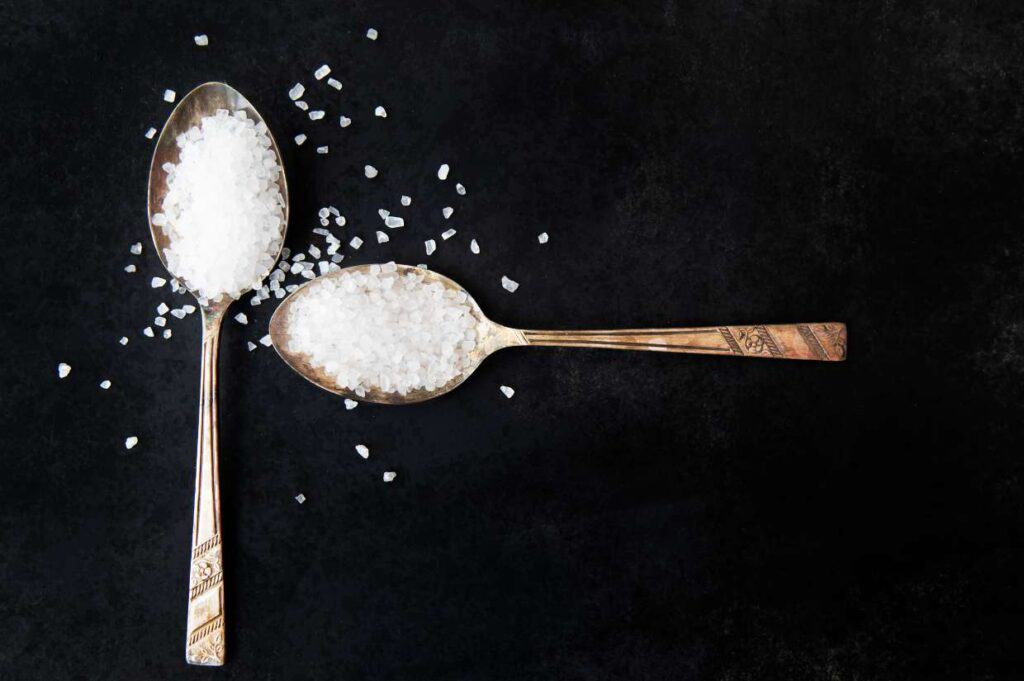 Two spoons with coarse salt on a black background.