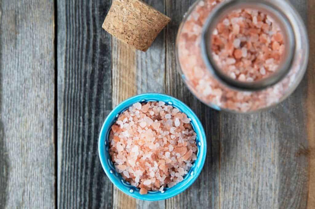 A bowl of pink salt on a wooden table.