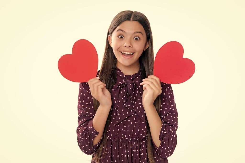 A young girl holding up two red heart shaped papers.