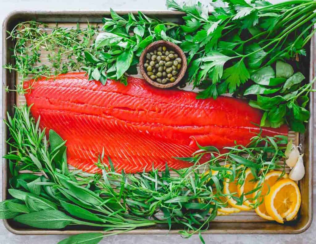A wild salmon fillet on a baking sheet with herbs.
