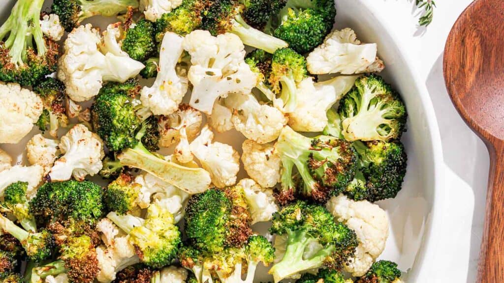 Roasted cauliflower and broccoli in a white bowl with a wooden spoon.