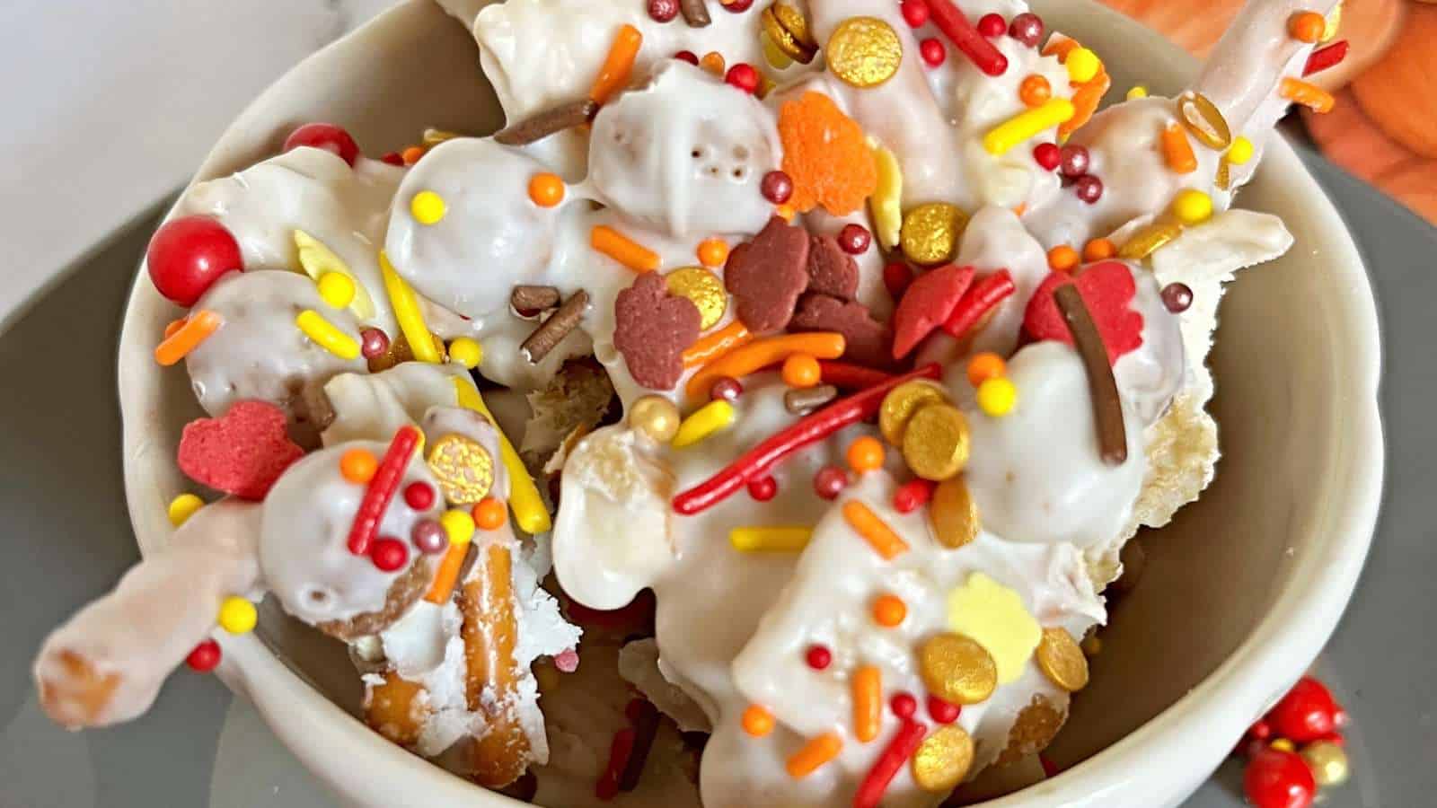 A white bowl filled with almond bark with candy and cereal.