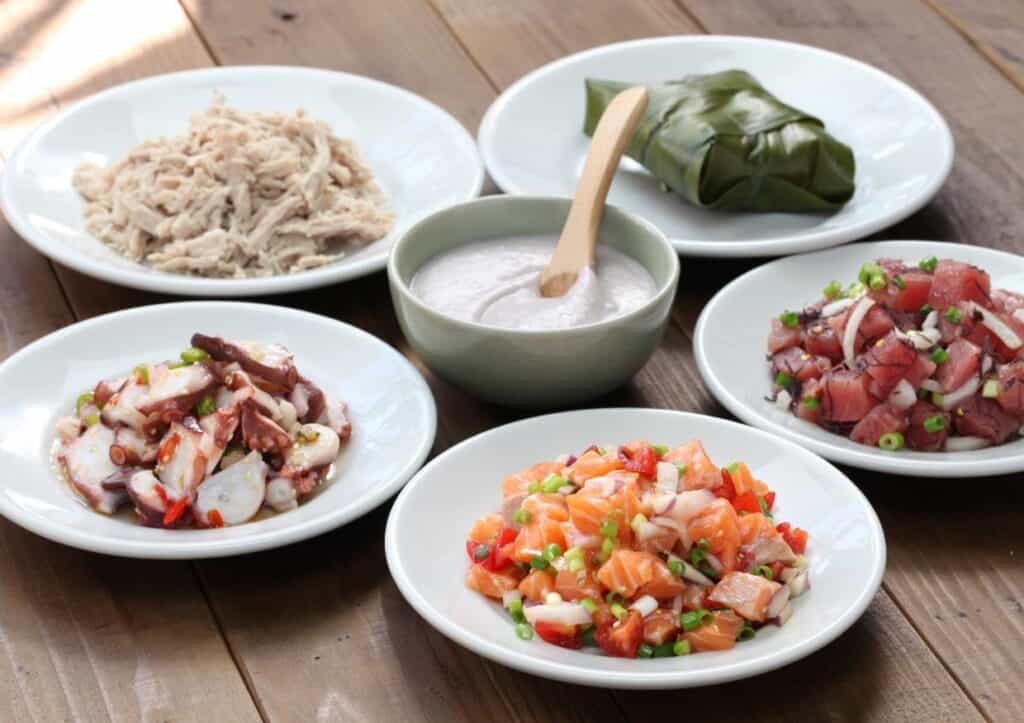 Four bowls with different types of Hawaiian luau food on a wooden table.