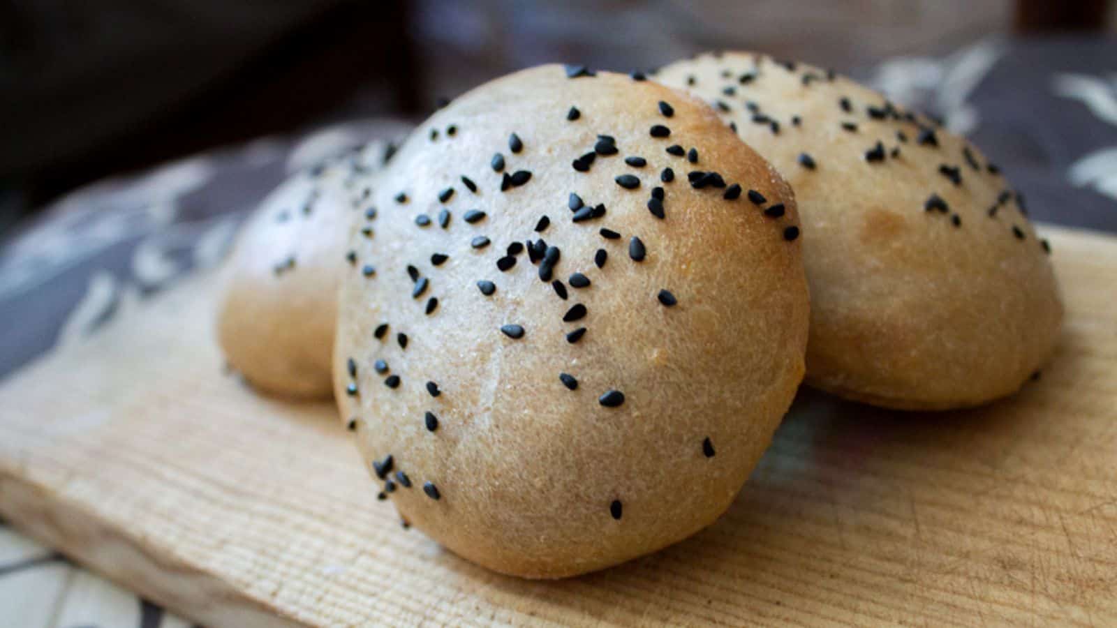 Sesame buns with sesame seeds on a wooden cutting board.