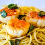 A serving of pasta topped with a seared scallops and a sage brown butter sauce.