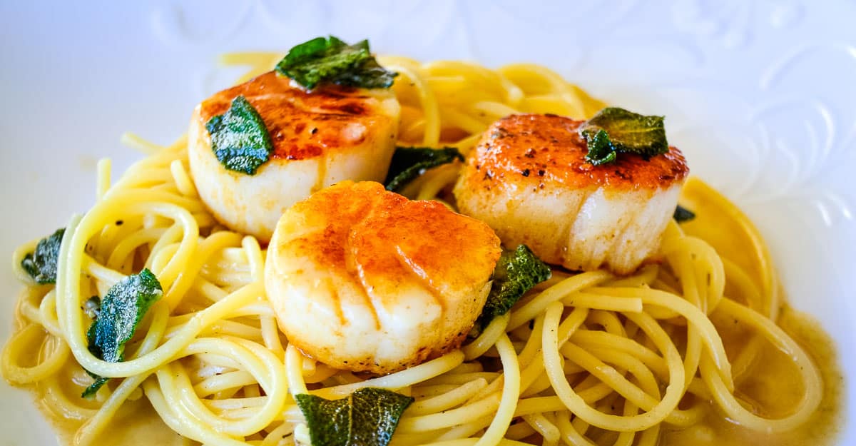A serving of pasta topped with a seared scallops and a sage brown butter sauce.