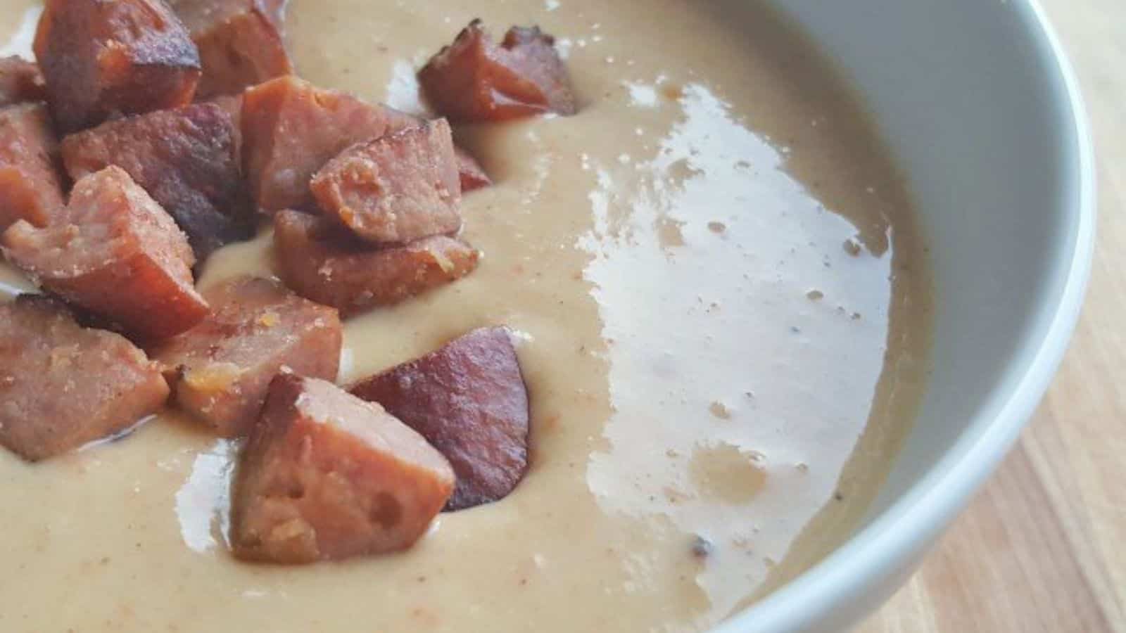 Image shows a closeup of a bowl of cheese and sausage soup with chopped sausage on top.