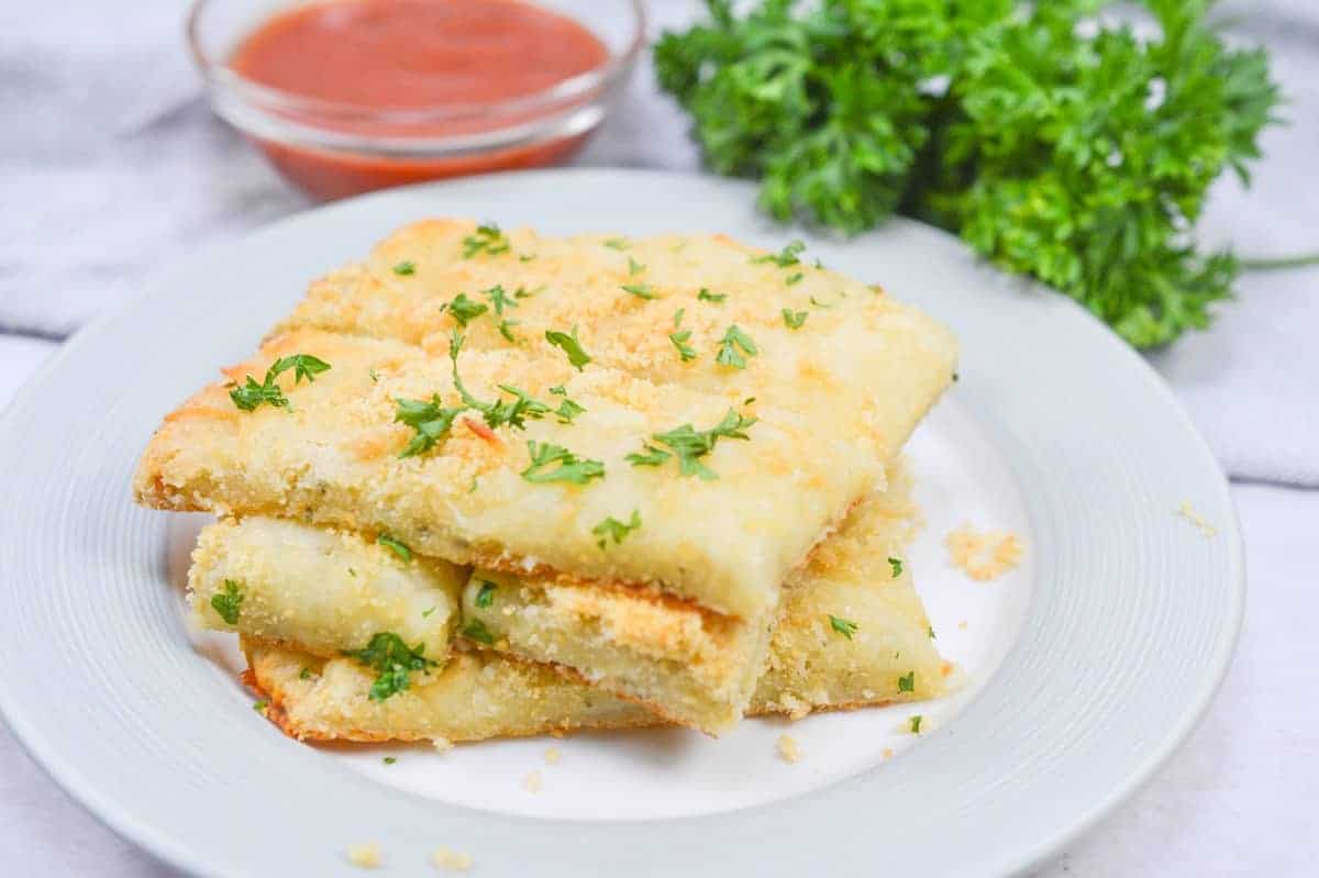 Cheesy bread sticks with marinara sauce and parsley on a plate.