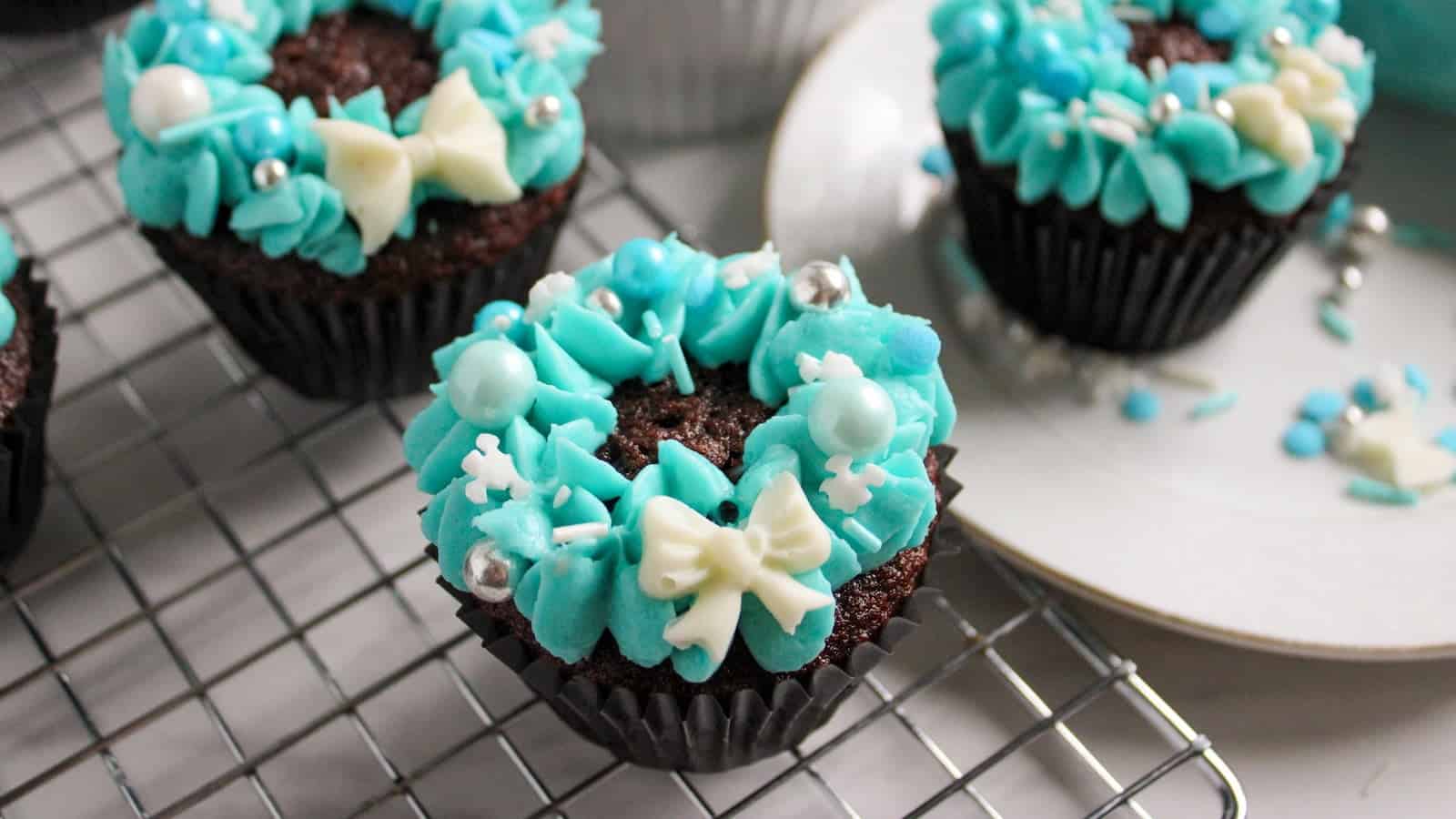 Christmas wreath cupcakes decorated with blue frosting on a cooling rack.