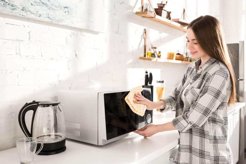 A woman is wiping down the outside of a microwave.