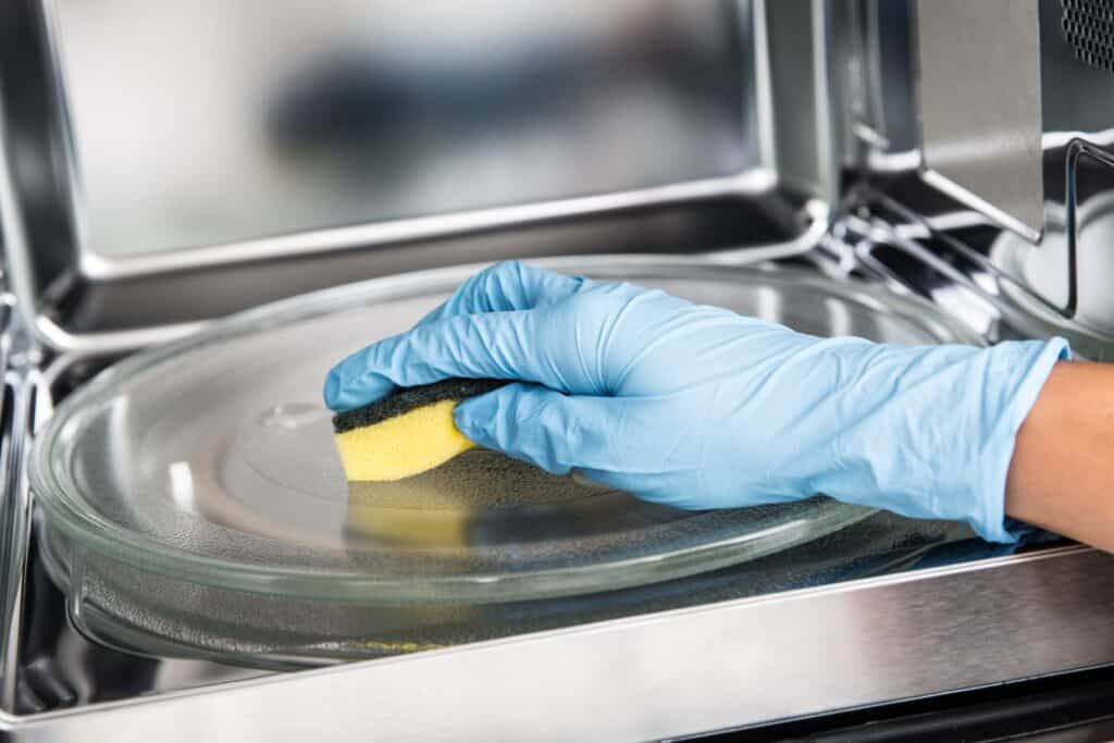 A person wearing blue gloves cleaning the inside of a microwave.