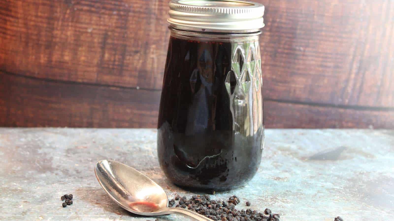 A jar of elderberry syrup with a spoon next to it.