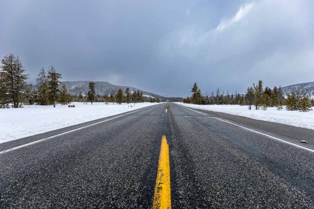 An empty road covered in snow, surrounded by trees in the background and prepared with an emergency car kit.