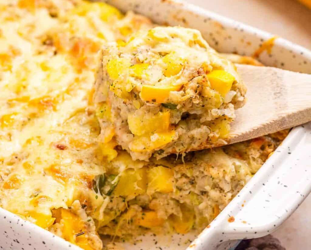 Squash casserole in a white dish with a wooden spoon.