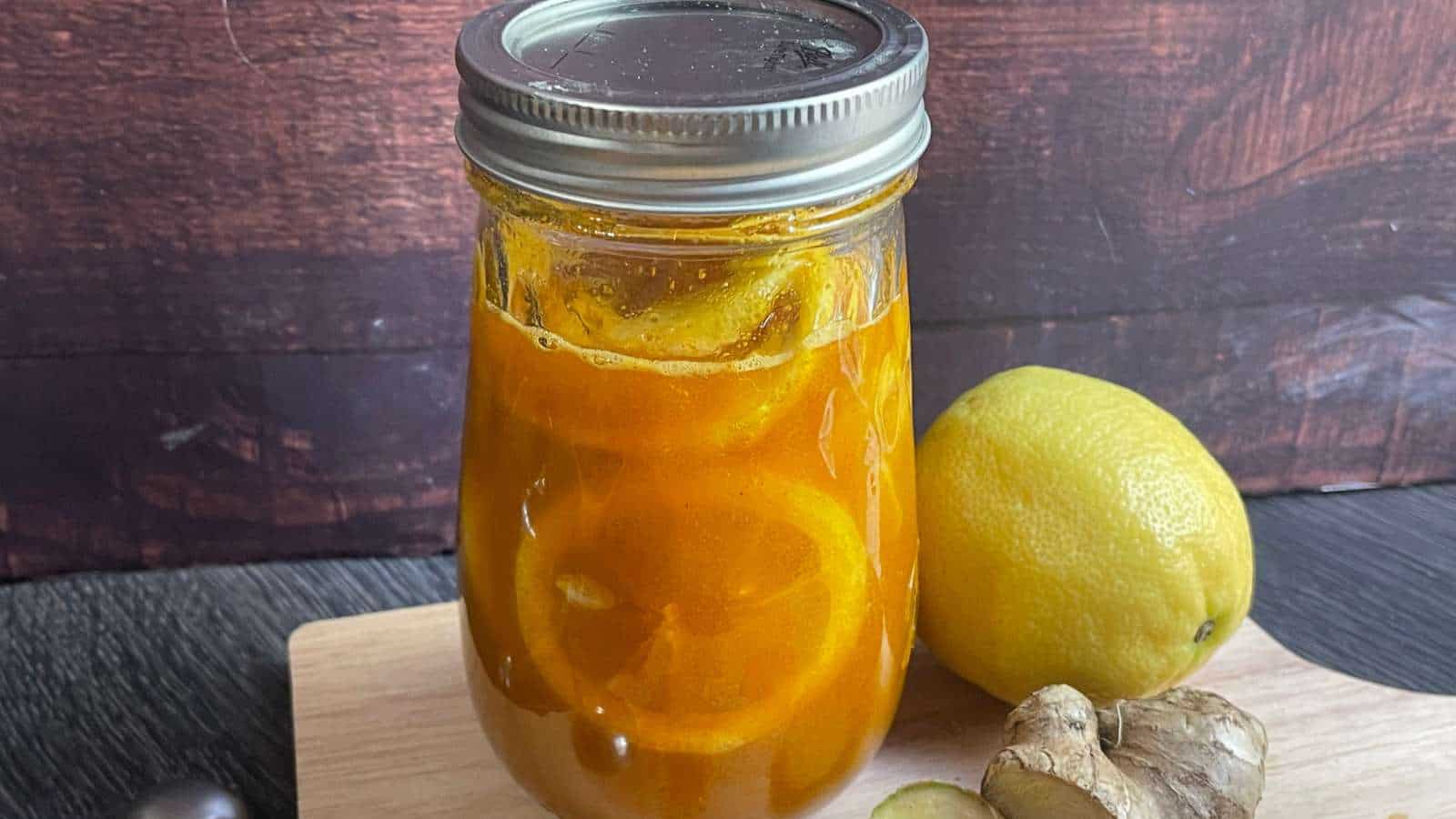 A mason jar ginger lemon syrup and  with lemons and ginger on a cutting board.