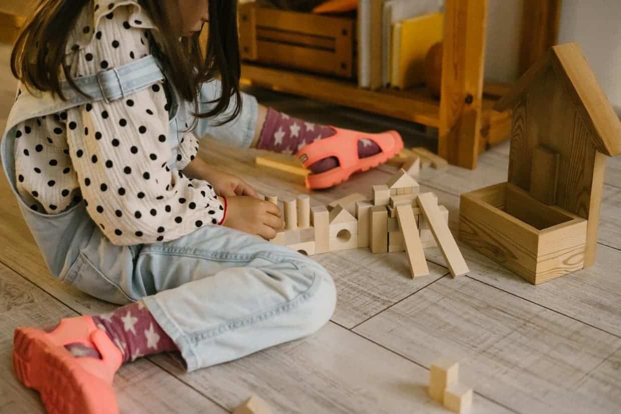 A little girl playing with wooden blocks on the floor.