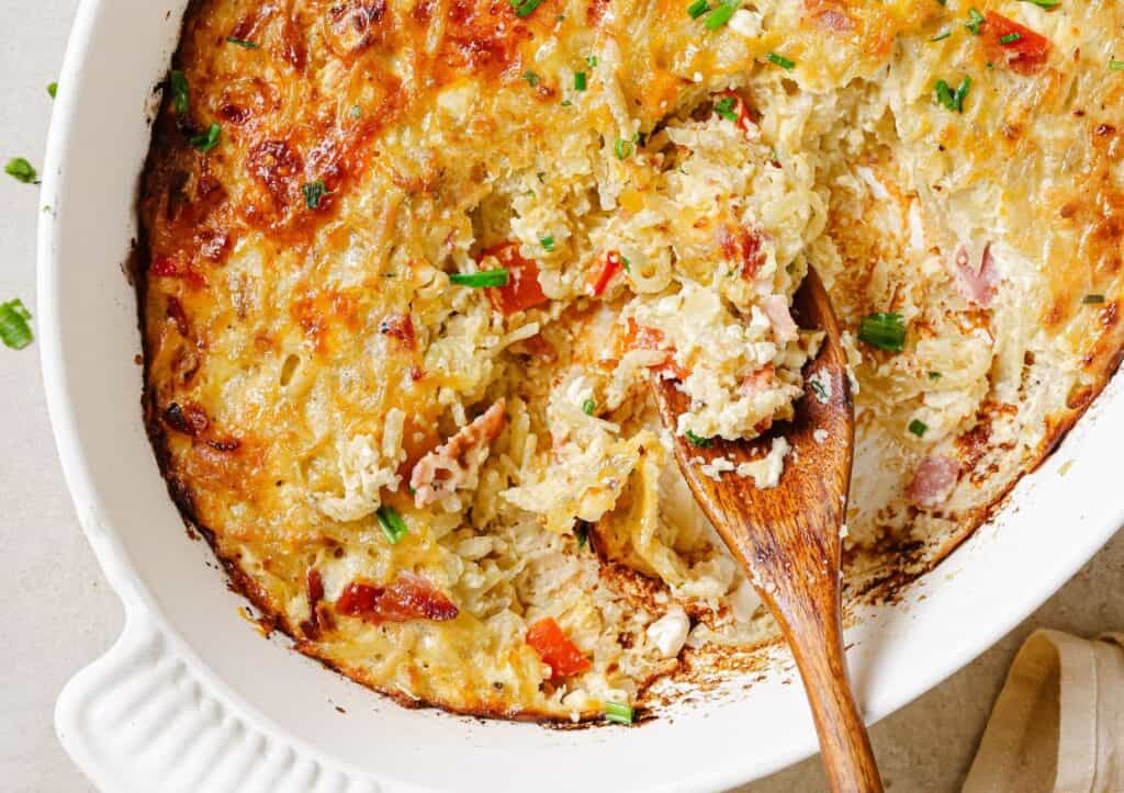 Hash brown breakfast casserole in a white dish with a wooden spoon.