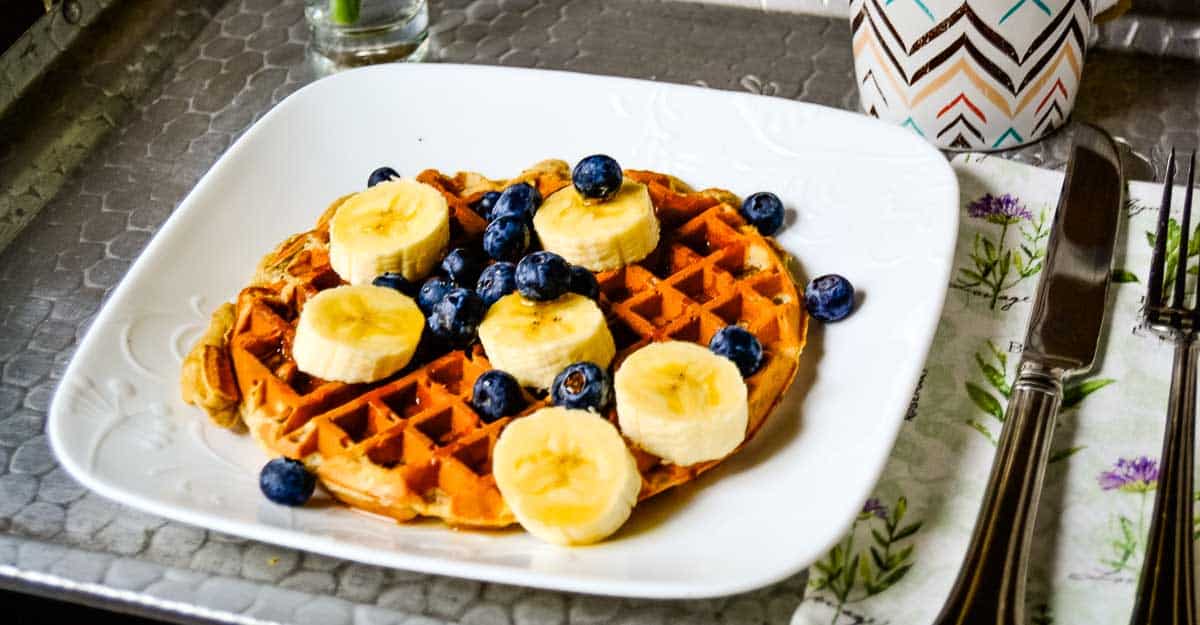 A plate of banana waffles with bananas and blueberries.