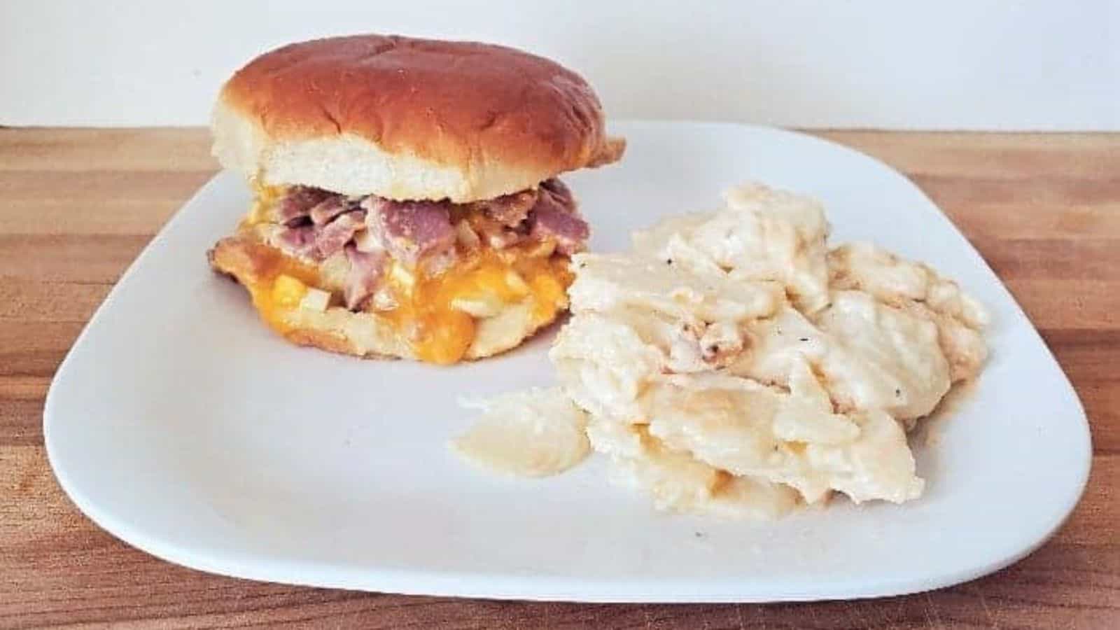 Image shows a white plate with a hot ham salad sandwich and scalloped potatoes.
