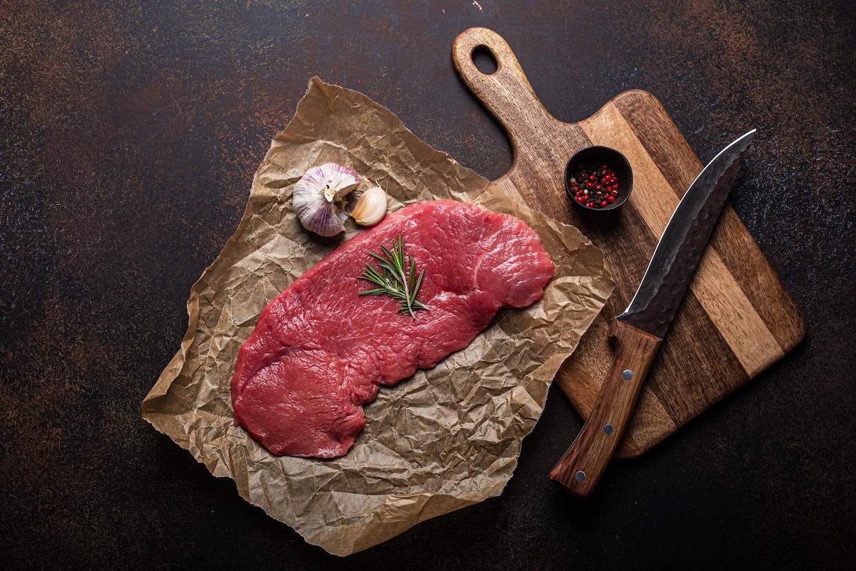 Raw beef on a cutting board with spices and a knife.