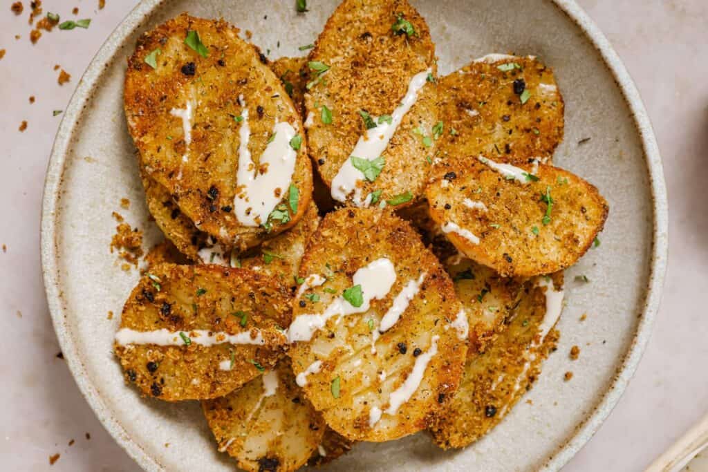 Parmesan crusted potatoes on a plate with sauce drizzled on top.