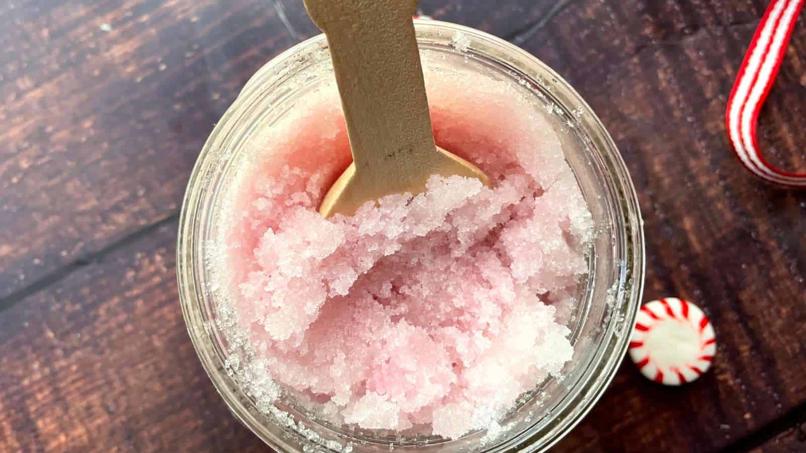 A mason jar of peppermint foot scrub with a wooden spoon and candy canes.