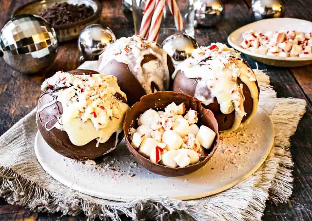 Four peppermint hot chocolate bombs on a plate, with an open hot chocolate bomb in the middle to show the inside.