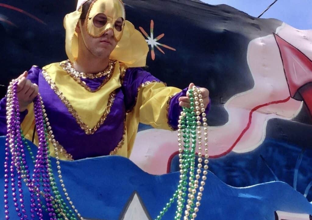 A woman in a mardi gras costume holds beads on a float.