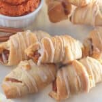 Mini pumpkin crescent rolls with dipping sauce on a plate.