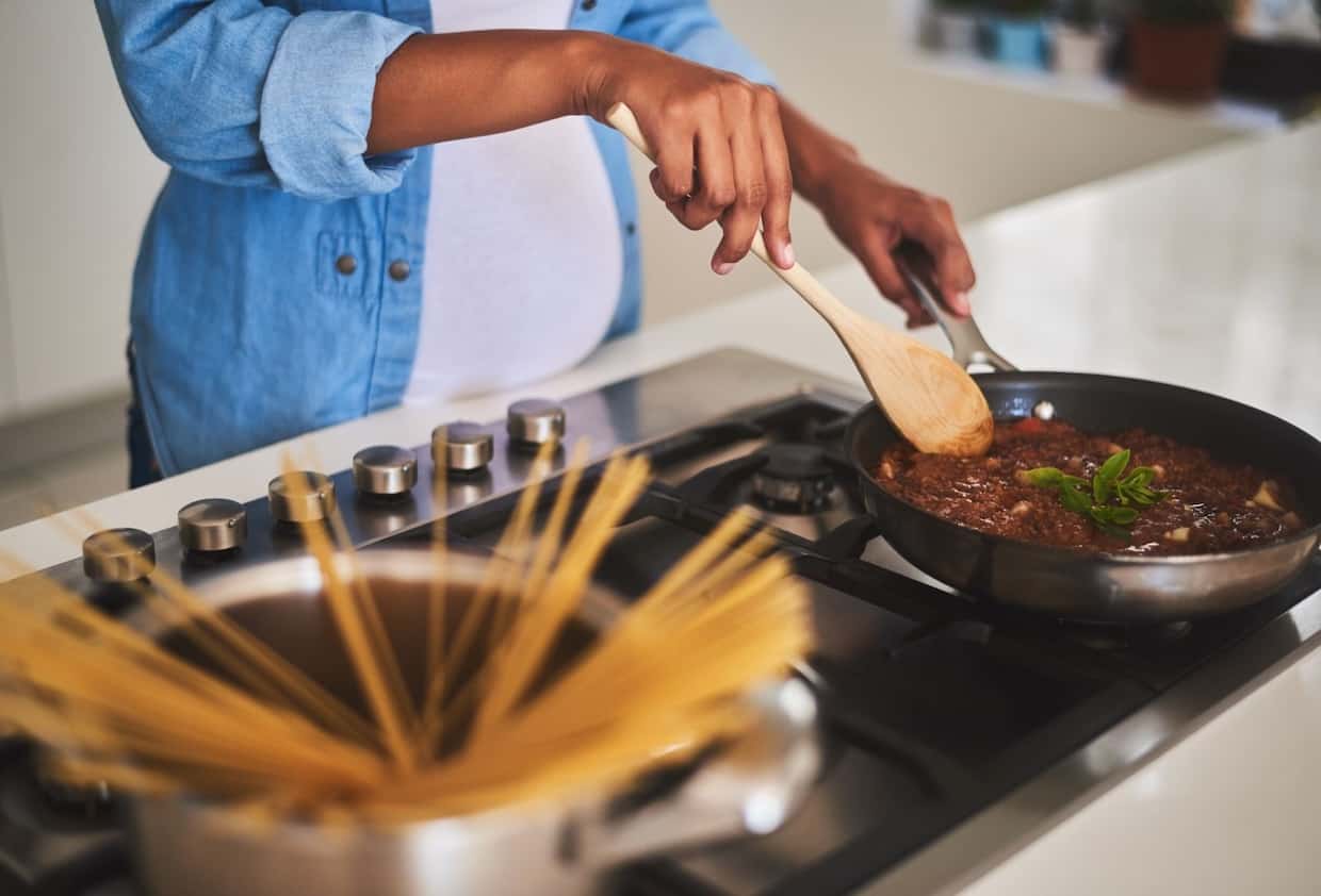 A pregnant woman is cooking rich-in-iron food in a pan on the stove.