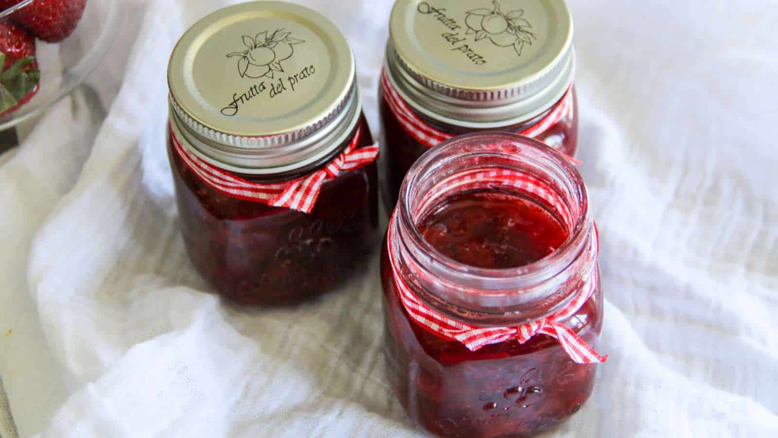 Strawberry syrup in mason jars on a white cloth.