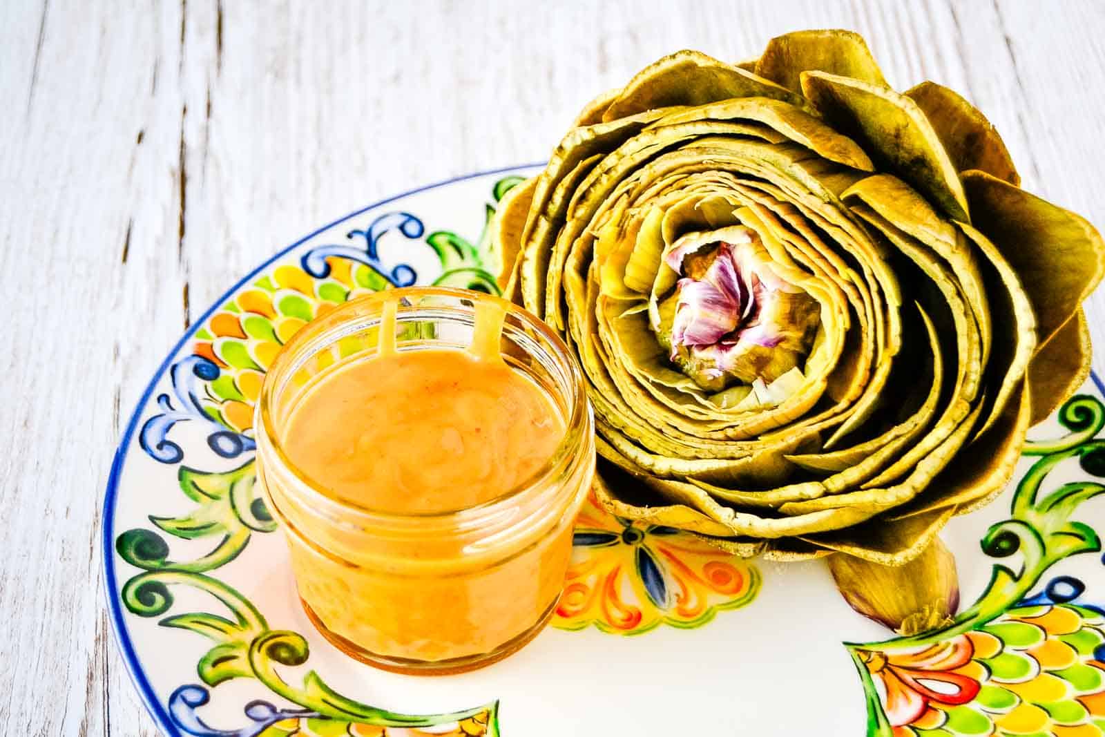 Artichoke with tangy orange sauce served on a plate.