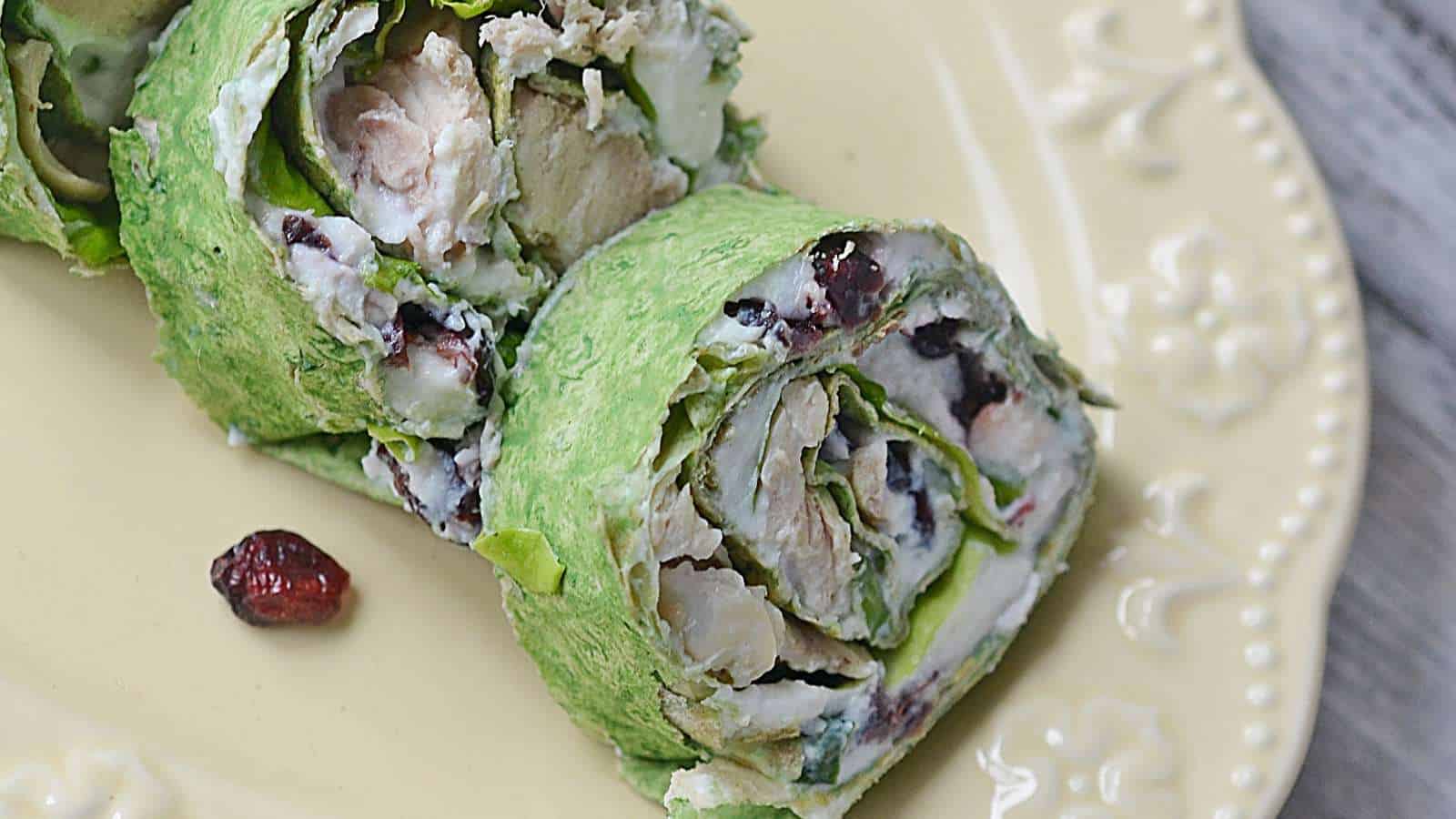 A plate with a green wrap with cranberries and turkey on it.
