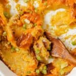 Cheesy potato casserole in a white dish with a wooden spoon.