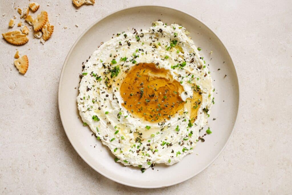 A plate with whipped feta with honey dip and crackers on it.