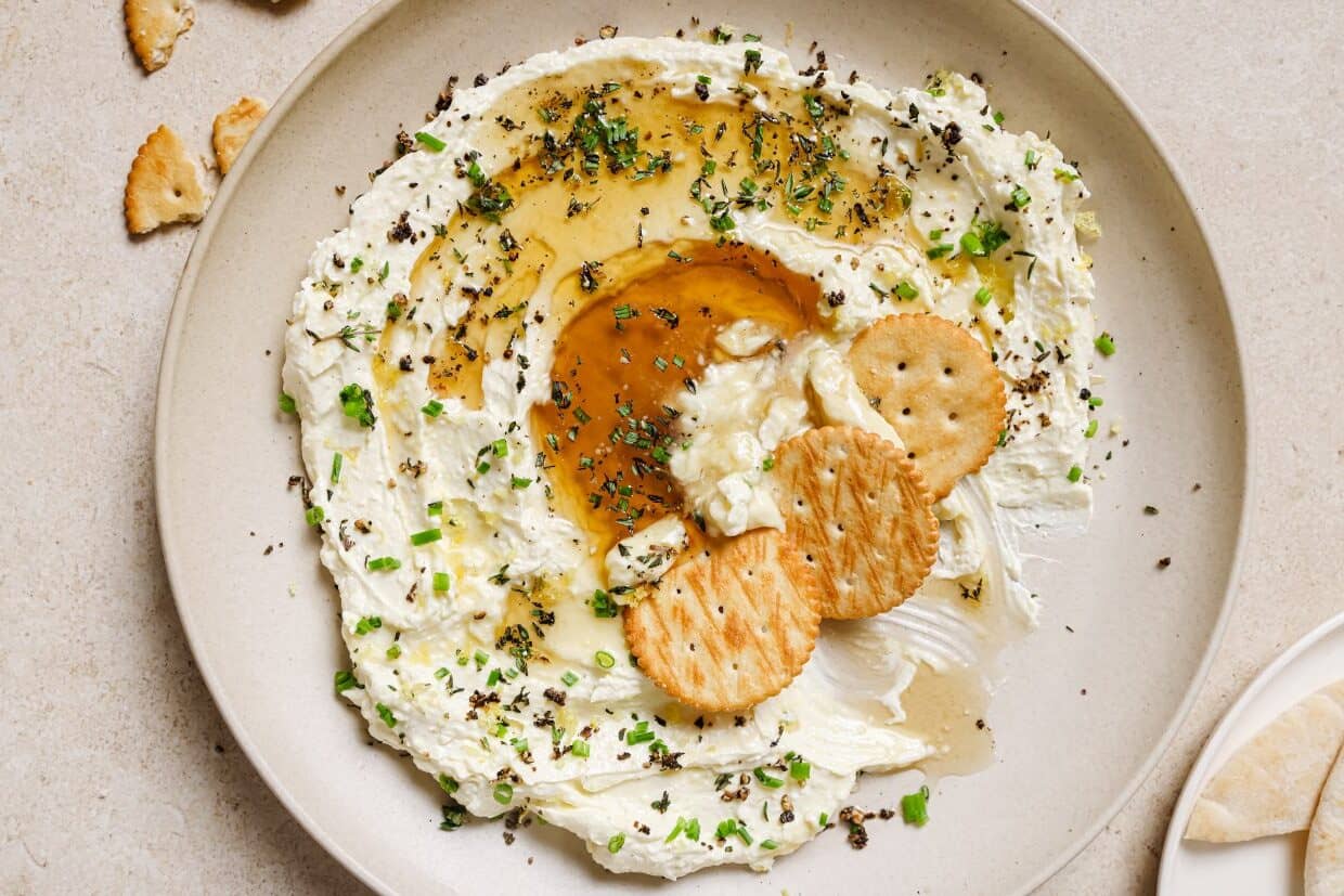A plate of whipped feta with honey dip and crackers on it.