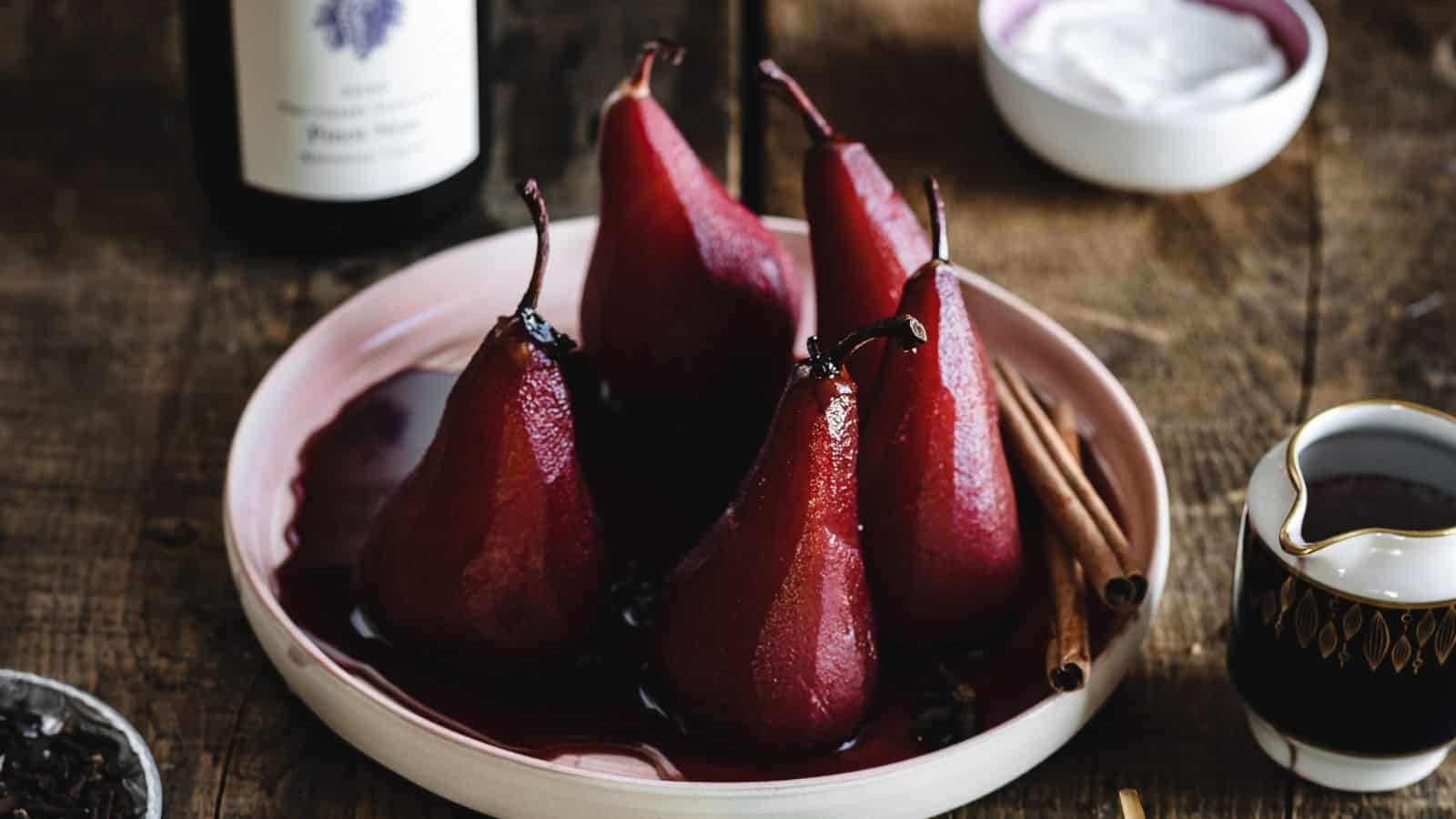 Poached pears on a pink plate with cinnamon sticks.