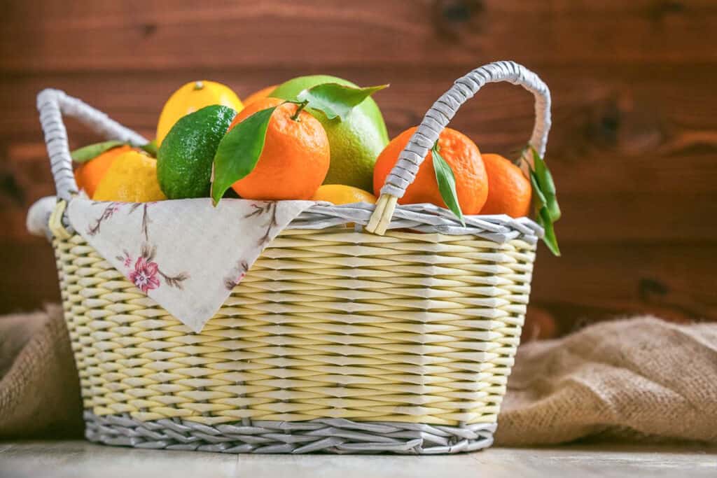 A basket full of oranges, limes and lemons on a wooden table.