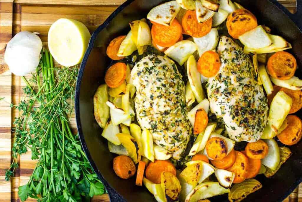 A dark skillet with chicken, carrots, parsnips, golden beets and herbs.