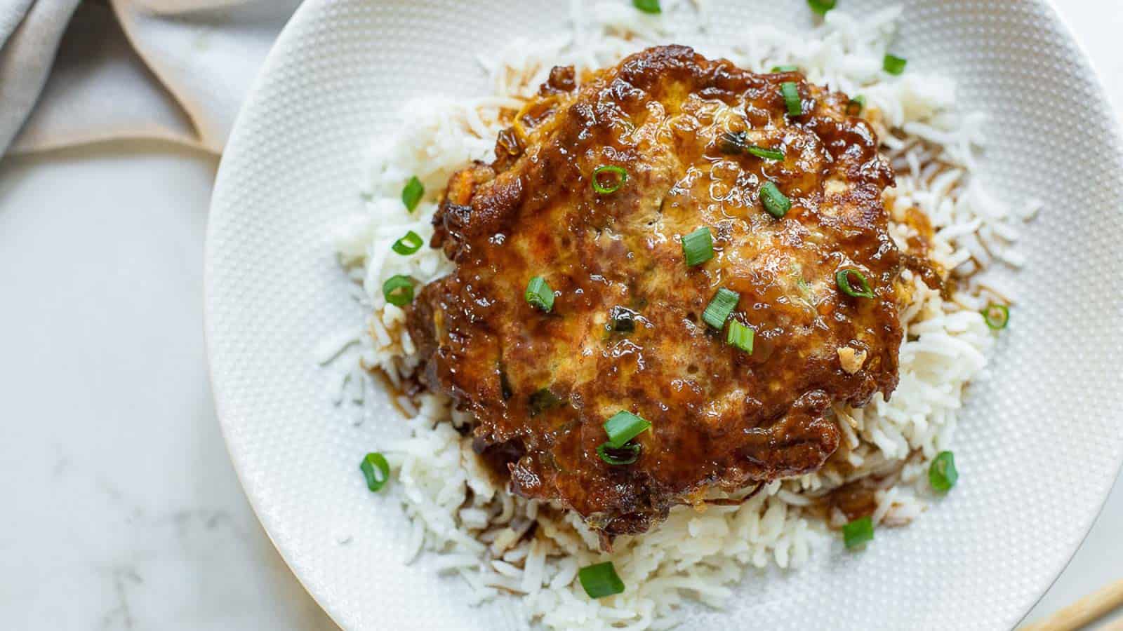 Chicken egg foo young on top of rice on a white plate.