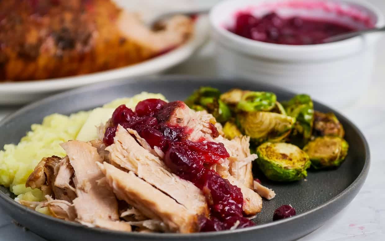 A plate with roasted pork, brussels sprouts and cranberry sauce.