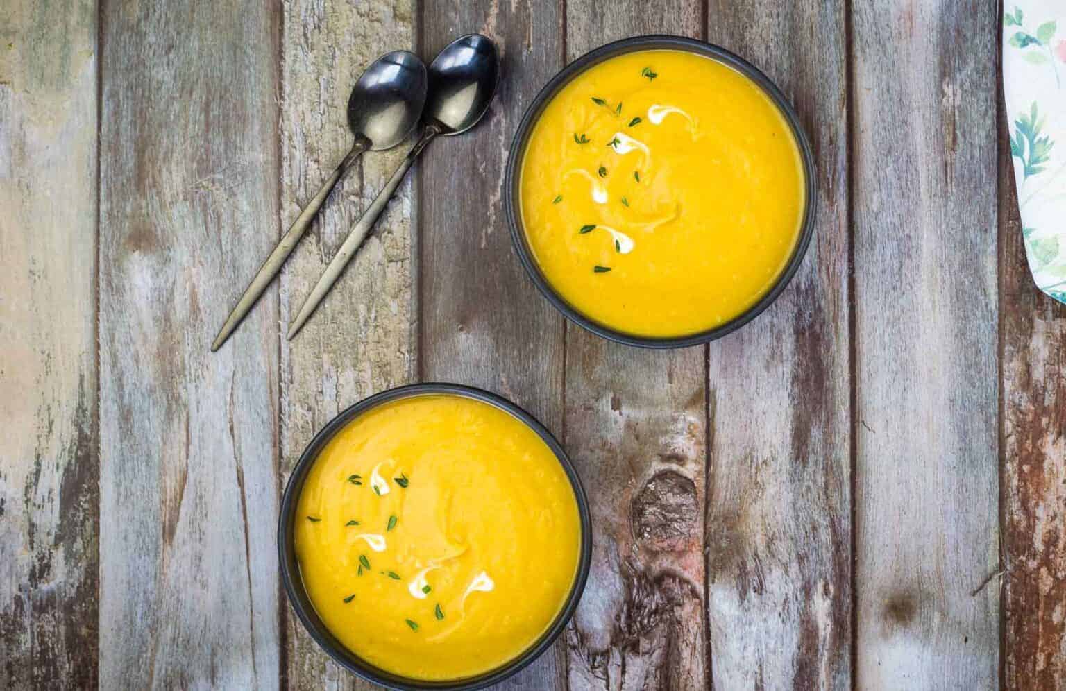 Two bowls of cream of butternut squash and sweet potato soup on a wooden table.