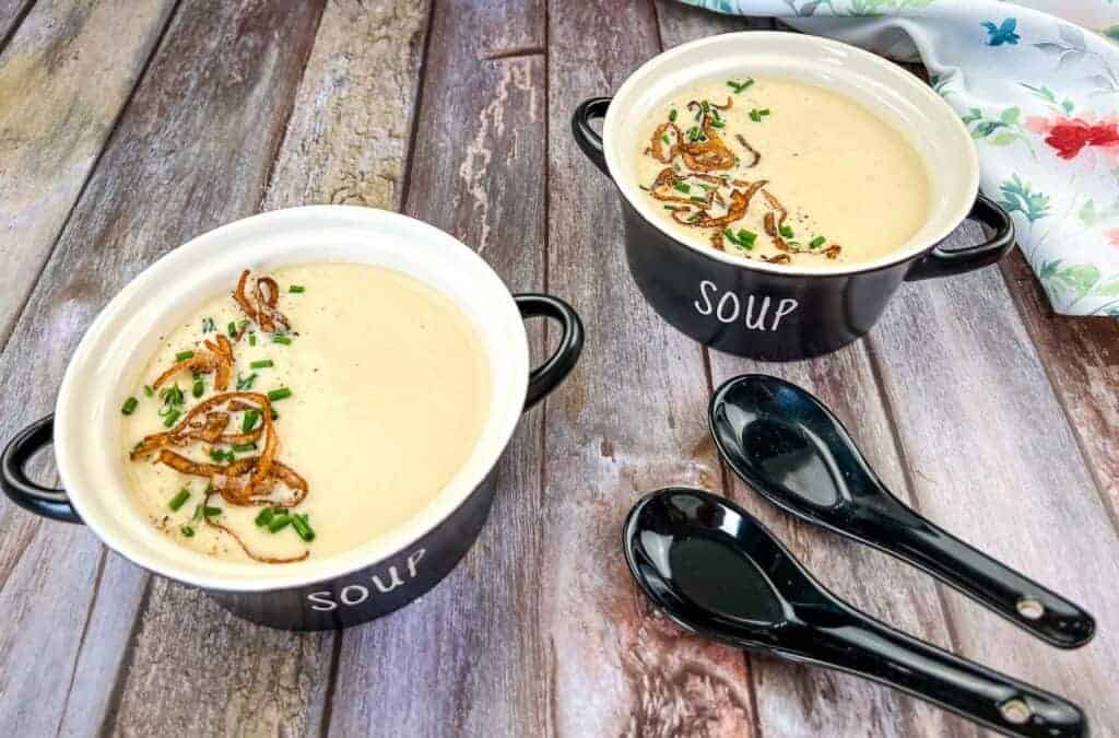 Two bowls of cream onion soup on a wooden table.