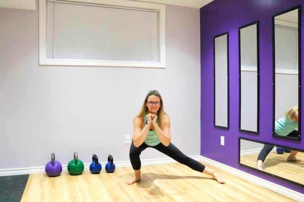 An effortless woman in a vivid purple room engaged in a squat during one of her quick and simple at-home workouts.