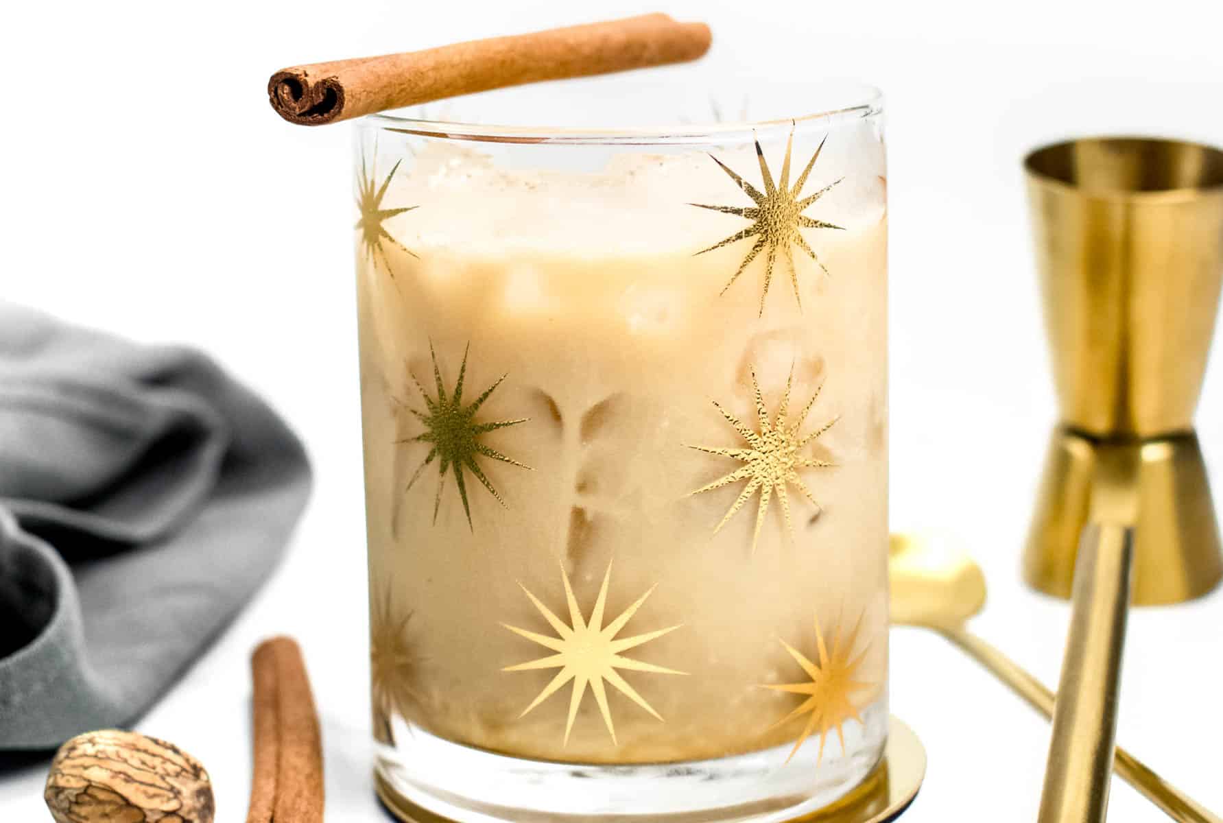A glass of eggnog cocktail with cinnamon sticks and nutmeg.